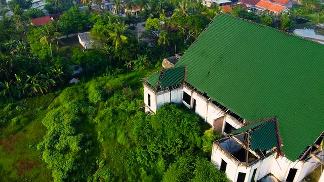 BEKASI, INDONESIA, JAN 2020 : Aerial, Tilt up, Drone Shot, above on abandoned farmhouse surrounded by paddy rice field, in the city of Bekasi, on a sunny, summer day. 2.7K resolution video