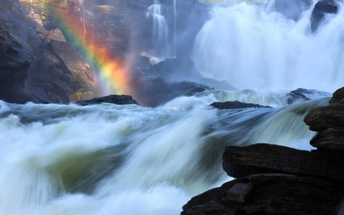 Raging river creates rainbow where steam meets the sunlight. - 318705952