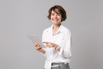 Smiling young business woman in white shirt posing isolated on grey wall background studio portrait. Achievement career wealth business concept. Mock up copy space. Holding, using tablet pc computer.