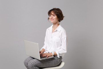 Beautiful young business woman in white shirt isolated on grey wall background studio portrait. Achievement career wealth business concept. Mock up copy space. Working on laptop pc computer, sitting.