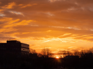 Silhouette of a building surrounded by trees at sunset, Warm glowing cloudy sky.