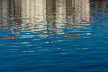 Water with small waves. Reflections of blue sky and buildings.