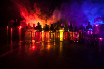 Smoke clouds and vape liquid bottles on dark background. Light effects. Useful as background or vape advertisement or vape background. Selective focus