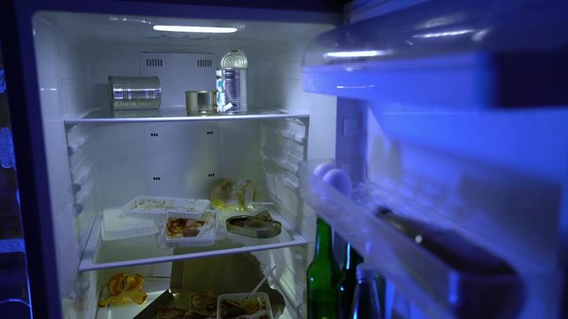 Leftover food in the fridge. Someone opens the refrigerator door. Dirty fridge full of stale food. The bachelor’s fridge. Night hunger. Improper nutrition. Scraps. Fast food. Junk food.
