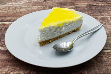 Slice of lemon cheesecake on white plate, wooden table