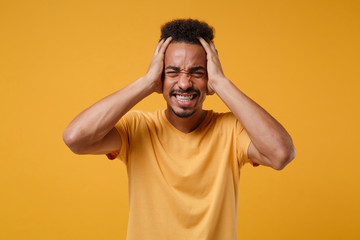Fototapeta na wymiar Frustrated young african american guy in casual t-shirt posing isolated on yellow orange wall background. People emotions lifestyle concept. Mock up copy space. Keeping eyes closed, put hands on head.