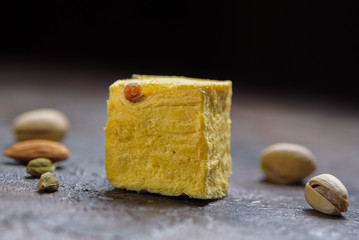 One cube of dessert soan papdi, cardamom grains, pistachios and almond on concrete kitchen surface.