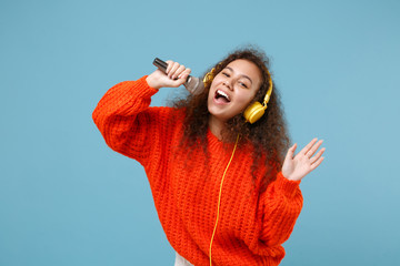Cheerful young african american girl in orange knitted clothes isolated on pastel blue background....