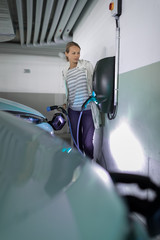 Young woman charging an electric vehicle in an underground garage equiped with e-car charger. Car...