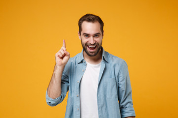 Excited young bearded man in casual blue shirt posing isolated on yellow orange background studio...