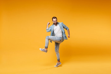 Fototapeta na wymiar Joyful young bearded man in casual blue shirt posing isolated on yellow orange background studio portrait. People sincere emotions lifestyle concept. Mock up copy space. Clenching fists like winner.