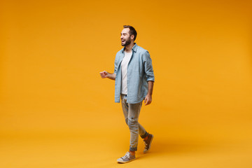 Cheerful laughing young bearded man in casual blue shirt posing isolated on yellow orange wall background studio portrait. People sincere emotions lifestyle concept. Mock up copy space. Looking aside.