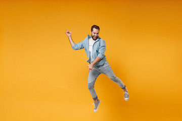 Fototapeta na wymiar Funny young bearded man in casual blue shirt posing isolated on yellow orange wall background studio portrait. People lifestyle concept. Mock up copy space. Jumping fooling around like playing guitar.