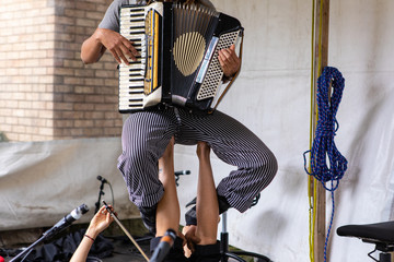 Midsection of female artist in stripped pant playing accordion and sitting on musician legs against...