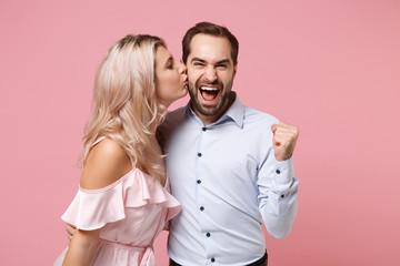 Young couple two guy girl in party outfit celebrating isolated on pastel pink background. People lifestyle Valentine's Day Women's Day birthday holiday concept. Kissing in cheek, doing winner gesture.