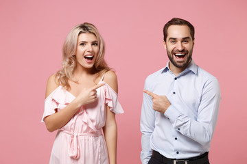 Excited young couple two guy girl in party outfit celebrating posing isolated on pastel pink background. Valentine's Day Women's Day birthday holiday concept. Pointing index fingers at each other.