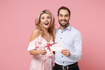 Cheerful young couple two guy girl in party outfit celebrating posing isolated on pastel pink...