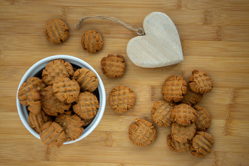 Very tasty peanut butter biscuits on bamboo wooden board in white baking bowl and decorative wood heart, golden baked healthy