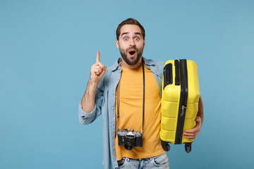 Traveler tourist man in summer clothes with photo camera isolated on blue background. Male passenger traveling abroad on weekends. Air flight journey. Hold suitcase, pointing finger up with new idea.