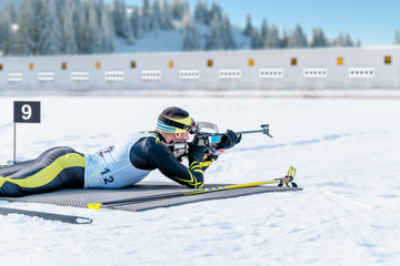 Biathlete lies and shoots a target at a 20 km race. Athlete with modern sports equipment for...