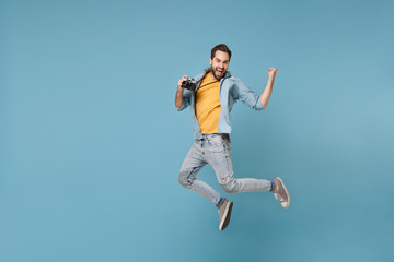Fototapeta na wymiar Happy traveler tourist man in yellow summer clothes with photo camera isolated on blue background. Male passenger traveling abroad on weekend. Air flight journey concept. Jumping doing winner gesture.