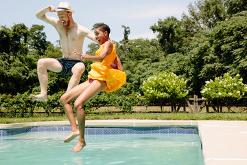 Interracial couple jumping into blue water in pool during the summer 