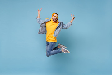 Fototapeta na wymiar Cheerful young hipster guy in fashion jeans denim clothes posing isolated on pastel blue background in studio. People lifestyle concept. Mock up copy space. Jumping, screaming, showing victory sign.