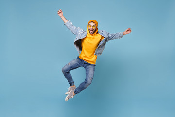 Fototapeta na wymiar Excited young hipster guy in fashion jeans denim clothes posing isolated on pastel blue wall background studio portrait. People emotions lifestyle concept. Mock up copy space. Jumping spreading hands.