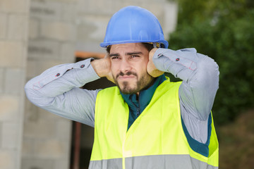 young construction worker covering ears