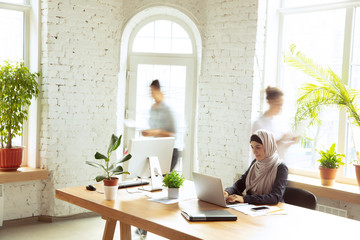 Concentrated. Portrait of a beautiful arabian businesswoman wearing hijab while working at openspace or office. Concept of occupation, freedom in business area, leadership, success, modern solution.
