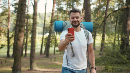 Handsome man with beard and backpack in forest uses speak on phone camera show around gps...