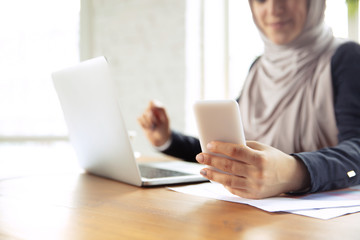 Using gadgets. Portrait of a beautiful arabian businesswoman wearing hijab while working at openspace or office. Concept of occupation, freedom in business area, leadership, success, modern solution.