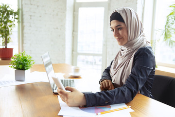 Using gadgets. Portrait of a beautiful arabian businesswoman wearing hijab while working at openspace or office. Concept of occupation, freedom in business area, leadership, success, modern solution.