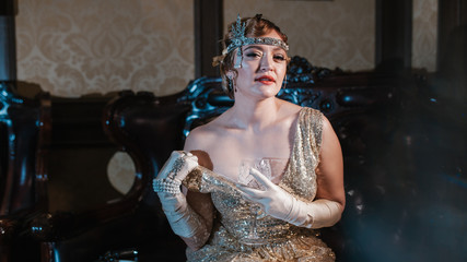a girl in a gold dress with a diadem on her head, sits on a leather chair, with one hand shows her...