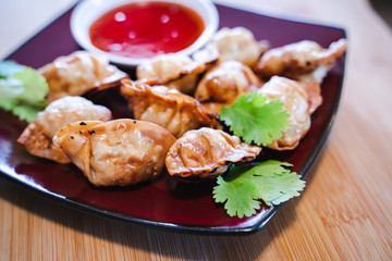 Crispy deep-fried wontons on wooden plate serve with sweet chilli sauce.