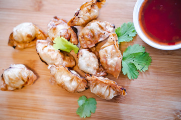 Crispy deep-fried wontons on wooden plate serve with sweet chilli sauce.