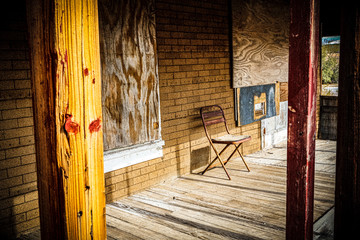 empty chair on porch of abandoned boarded up house