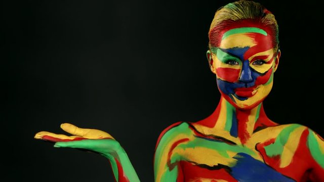 Woman with color face art and body paint. Girl with bright colorful makeup and bodyart pointing to looking right