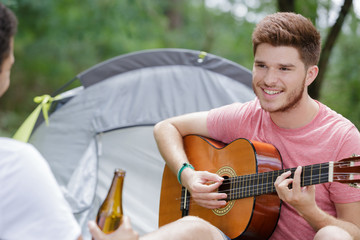 young man playing guitar beside his tent