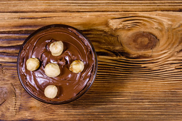 Glass bowl with chocolate spread and hazelnuts on a wooden table. Top view