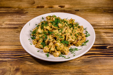 Plate with champignons stewed in sour cream on a wooden table