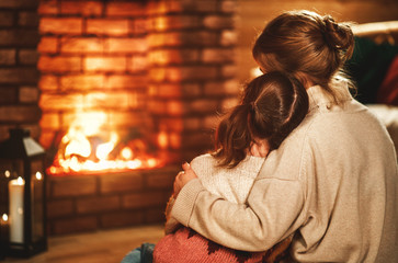 family mother and child reading book and drink tea on winter evening by fireplace