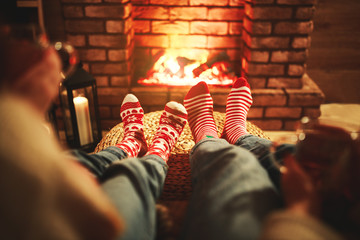 family mother and child warm their feet and drink tea on winter evening by fireplace