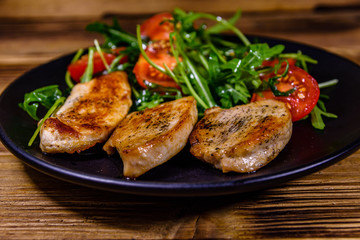 Roasted chicken breasts and salad with arugula and cherry tomatoes in a black plate