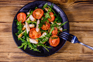 Roasted chicken breasts and salad with arugula and cherry tomatoes in a ceramic plate. Top view