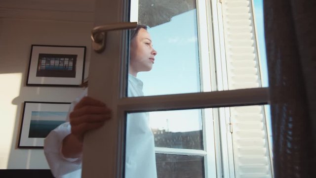Attractive girl opening a window to a balcony in the morning