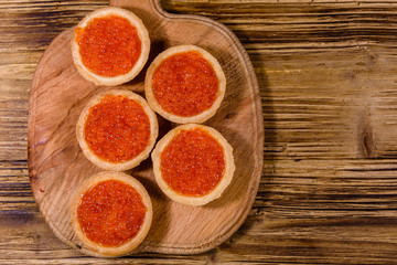 Tartlets with red caviar on a wooden cutting board. Festive food. Top view