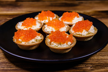 Tartlets with red caviar on a black plate. Festive food