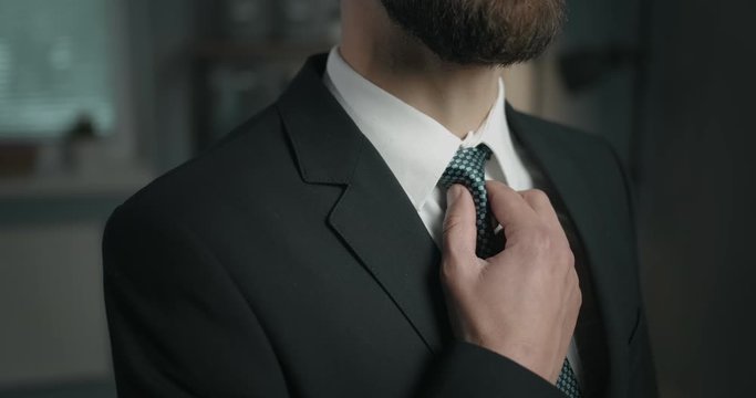 Bearded masculine businessman in black suit touching tie, closeup