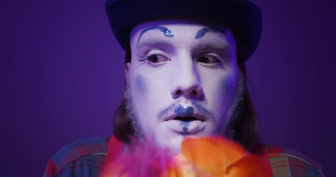 Close up face of colorful charismatic mime clown in a hat making trembling, nervous emotions and looks uncertainly at the camera. Isolated purple background